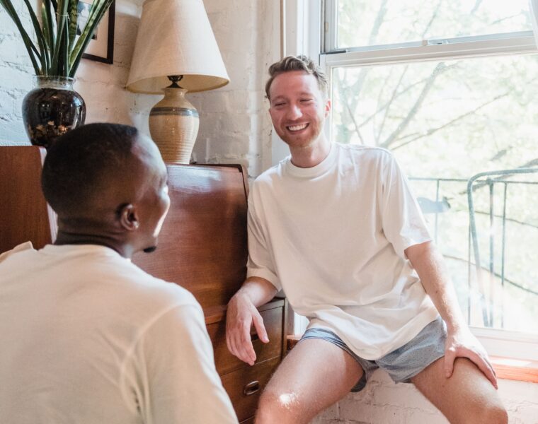 Two men smiling and talking together in a sunlit bedroom