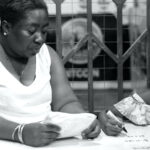 Black-and-white photograph of a woman holding an open exercise book beside a child holding a pen over a workbook.