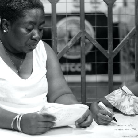 Black-and-white photograph of a woman holding an open exercise book beside a child holding a pen over a workbook.