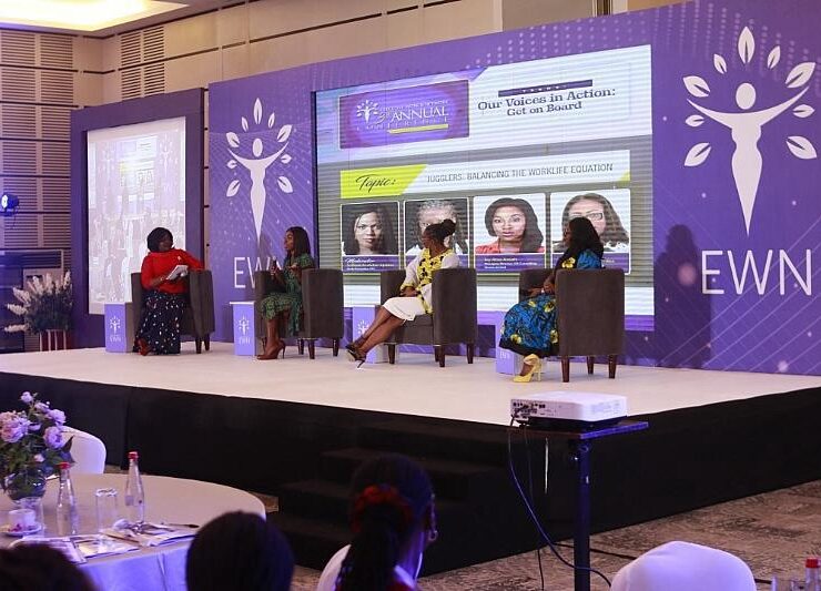 Four women seated on stage during a panel discussion against a purple EWN backdrop.